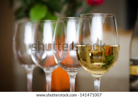 A wine glass with wine and 3 empty ones with a bottle and flowers on the background