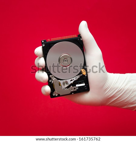 A hard disk being held by a scientist or repairman\'s hand on a red with valuable files awaiting to be recovered