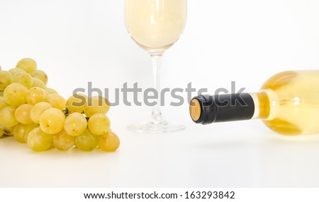 Yellow wine with a tilted bottle and grapes and a wine glass on the background