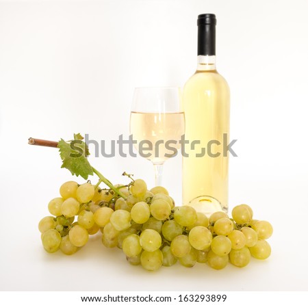 Yellow wine in a glass with grapes a bottle and a vine leaf