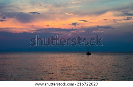 A beautiful sunset view of a fishing boat on calm ocean water with a bright orange blue sky and small waves suggesting calm freedom and peace