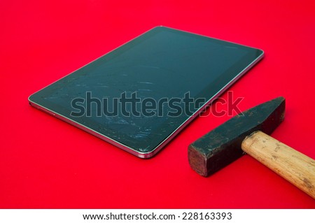 A hammer next to a broken touchscreen tablet on a red alerted important background suggesting expensive repairs for a modern piece of electronics which is broken