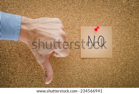 Thumbs down with a pinned red paper note with NO written and a business man hand showing refusal and denial with a contrast strong light suggesting a serious look