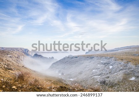 Entrance to a foggy valley with mist on a cold autumn-winter day with a blue sky and deserted landscape