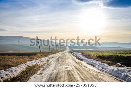 Rural countryside unpaved gravel road on a cold spring winter day with fields and snow and a contrasty filtered look