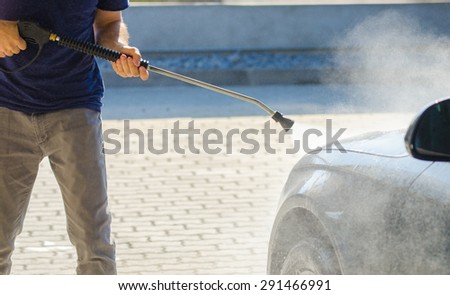 Man washing his car with a pressure cleaner with a blue look and lots of vapor