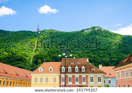 Brasov writing on the Tampa Hill with the fresh green forest and the cable route in the background and historic buildings on the foreground
