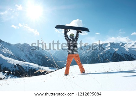 snowboarder raises a snowboard over his head, stands on the snow clear day,