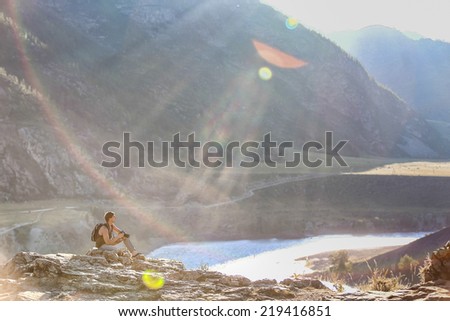 young man with a backpack, sitting on the edge of a cliff . sun