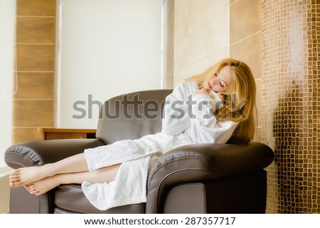 Beautiful blonde girl in a white robe basking in the chair