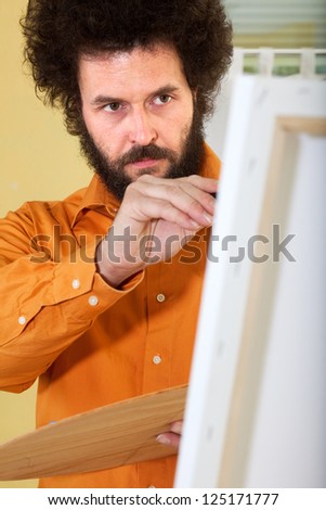 Mature painter in a bright, orange shirt, working in his studio on a painting.