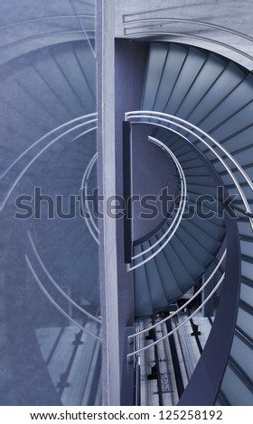 Round staircase built from glass and steel in a modern office building. Processed in blueish style to emphasize modern look.