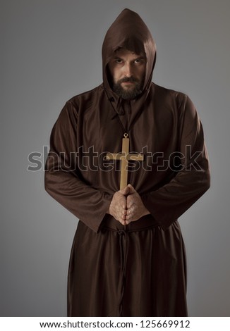 Studio shot of a man wearing a monk robe, holding his hands in praying pose while looking at camera.