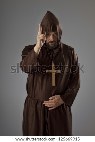 Studio shot of a man wearing a monk robe, holding his hand blessing someone while looking at camera.