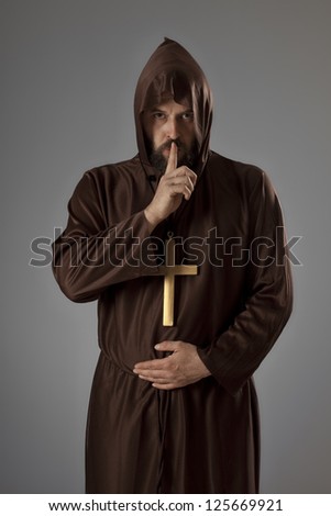 Studio shot of a man wearing a monk robe, holding a finger on his mouth, asking for silence while looking at camera.