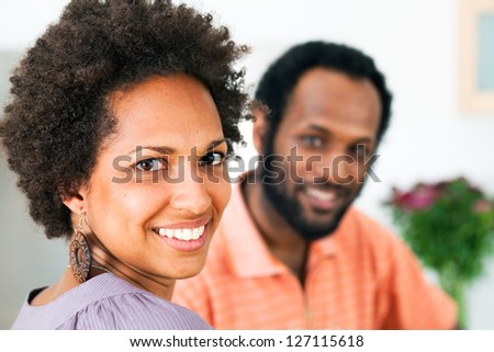 Young couple of African descent sitting in a home kitchen, enjoying each other\'s company. Focus on the girl looking into the camera..