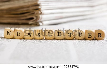 Concept of dices with letters forming word: Newsletter. Generic newspaper background with some blurred text on the bottom and paper stack in the back. Dices made from wood with natural imperfections.