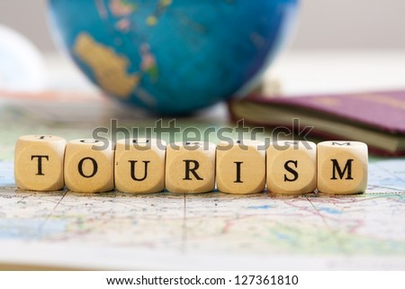 Concept of dices with letters forming words: Tourism. Blurred map, globe and passport as background.  Dices made from wood with natural imperfections.