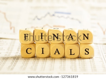 Concept of dices with letters forming word: Financials. On generic newspaper background with stock market numbers and some blurred charts.  Dices made from wood with natural imperfections.