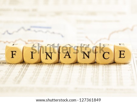 Concept of dices with letters forming word: Finance. On generic newspaper background with stock market numbers and some blurred charts.  Dices made from wood with natural imperfections