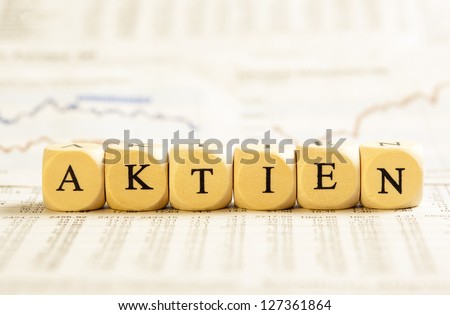 Concept of dices with letters forming word: Aktien - German for Stock. On generic newspaper background with stock market numbers and some blurred charts.