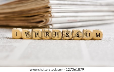 Concept of dices with letters forming word: Impressum (German for Imprint). Generic newspaper background with some blurred text on the bottom and paper stack in the back.
