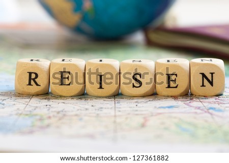 Concept of dices with letters forming words: Reisen (German for travel). Blurred map, globe and passport as background.  Dices made from wood with natural imperfections.