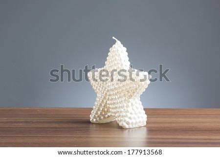 Single white candle in shape of a star on a wooden table.