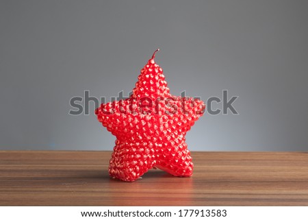 Single candle in shape of a star on a wooden table.