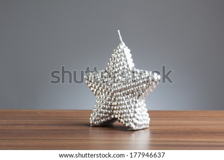 Single silver candle in shape of a star on a wooden table.