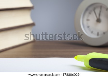 Black bullet pen, stack of books, clock and an empty sheet of paper.