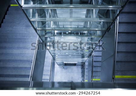 Glass elevator shaft and concrete staircase leading down towards an underground train station in Vienna, Austria.