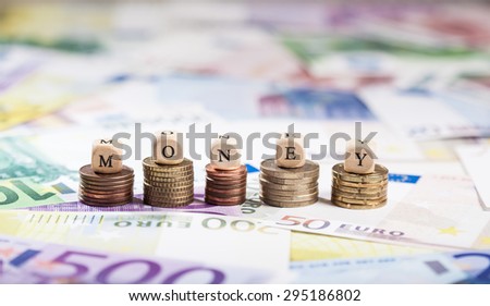 Cube letters building the term Money. Shallow depth of field, focus on coin stacks and letters.