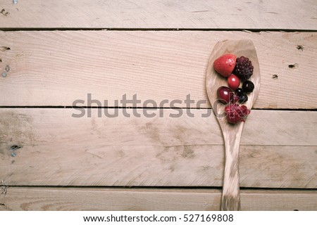 Red and blue berries on cooking spoon, high angle birds eye view on wood table planks.