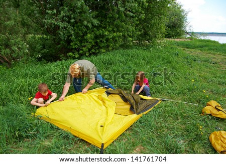 happy Father with children installing their tent on camping site.