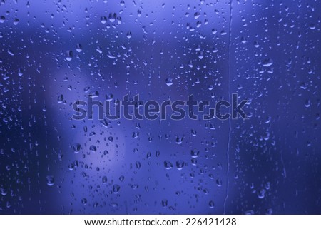 Rainy Days ,rain drops on glass window ,city lights  in the background blue