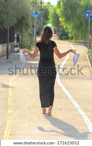 Barefoot brunette walking on the asphalt with shoes in hand