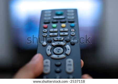 Closeup hand holding a TV remote control against the television