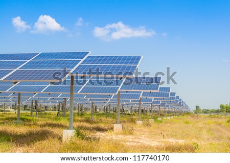 The field of solar panel with green grass in front of a blue sky with clouds.