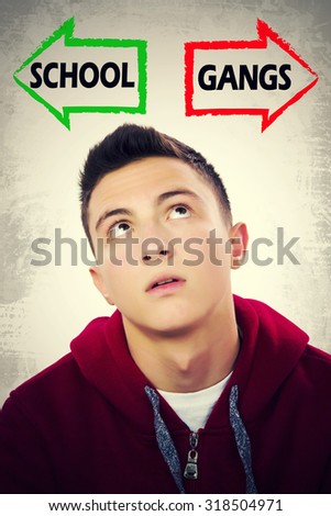 Portrait of handsome teenage boy thinking what to choose between SCHOOL and GANGS. Grunge background. Pointing arrows