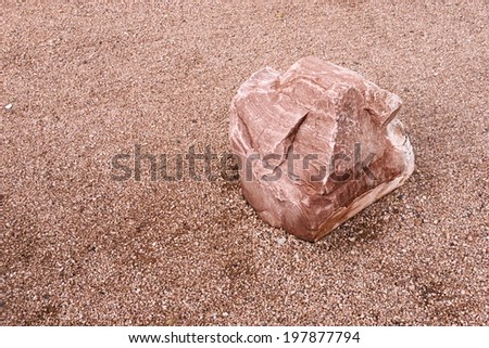 An image of a single red rock on a red gravel ground