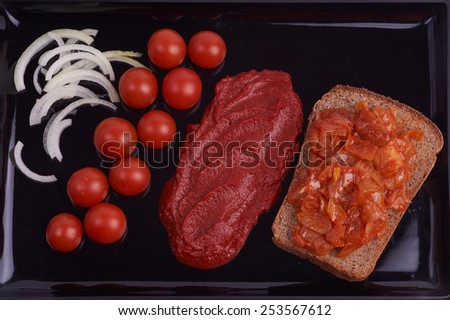 Fresh cherry tomatoes, onion and tomato paste on black tray. Red vegetarian food.