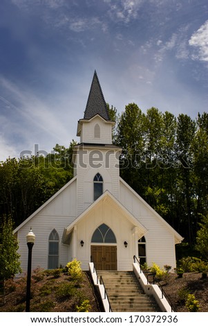 A vintage white church on the hill with steps going up to the front door.