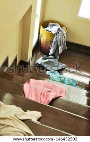 Lots of messy clothes on a cloth basket and stair wooden floor