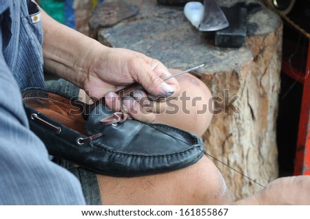man is repairing leather shoe; an occupation in Thailand