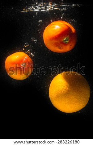 High speed photography of fruits & vegetables with splash in water isolated on black background - ORANGE & TOMATOES
