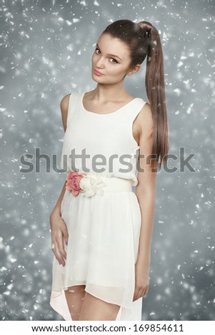 Young female with healthy shining brown hairs put in pony tail. White dress.