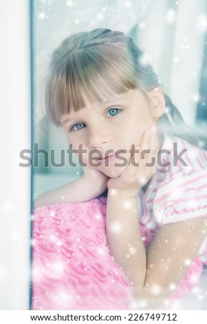 Little girl behind a window. It's snowing outside.