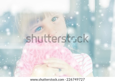 Little girl behind a window. It\'s snowing outside.