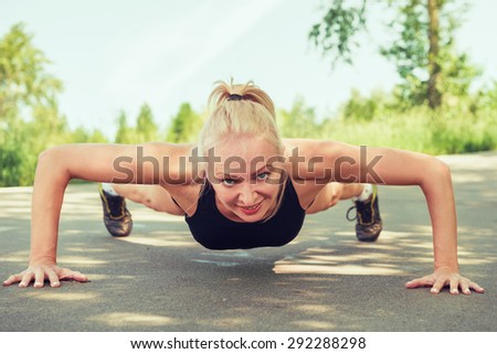 Young woman doing push ups outdoors in a park on sunny summer day. Girl in sportswear.